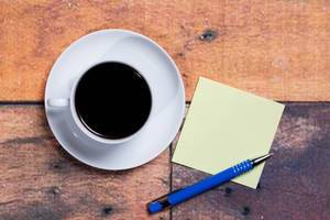 Cup of coffee and a sticky note with empty space for a text on wooden background