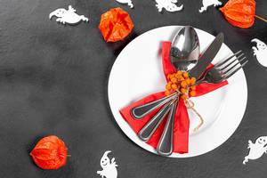 Cutlery on a black background with white ghosts and fruits of physalis. Table setting for Halloween