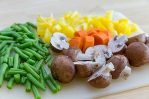 Cutting vegetables for oven-roasted vegetables: green beans, carrots, yellow bell pepers and mushrooms