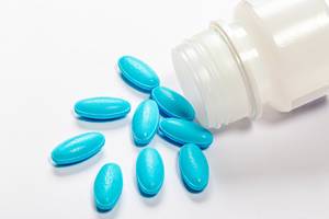 Das Konzept der medikamentösen Behandlung - Blaue Tabletten auf weißem Hintergrund und einer offenen Kunststoffverpackung