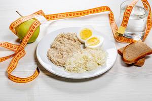 Das Konzept einer gesunden Ernährung mit geringen Kalorien - Lunch umgeben von einem Maßband auf weißem Holzhintergrund