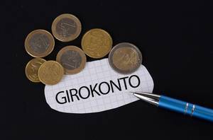 Das Konzept vom Girokonto: Girokonto Text auf einem Blatt Papier mit einigen Münzen und einem blauen Stift im schwarzen Hintergrund