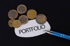 Das Konzept vom Portfolio: Portfolio Text auf einem Blatt Papier mit einigen Münzen und einem blauen Stift im schwarzen Hintergrund