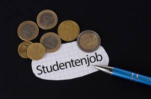 Das Konzept vom Studentenjob: Studentenjob Text auf einem Blatt Papier mit einigen Münzen und einem blauen Stift im schwarzen Hintergrund