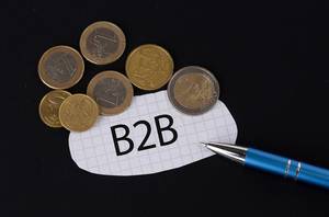 Das Konzept von B2B: B2B Text auf einem Blatt Papier mit einigen Münzen und einem blauen Stift im schwarzen Hintergrund
