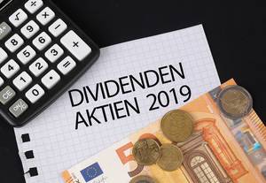 Das Konzept von Dividenden Aktien 2019: Dividenden Aktien 2019 Text auf einem Blatt Papier mit einigen Münzen, einem 5-Euro Schein und einem Kalkulator