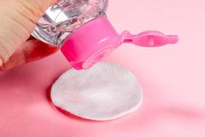 Das Konzept von Hautreinigung und Schminkentfernung: Mizellen-Wasser und Wattepads auf pinkem Hintergrund