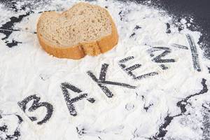 Das Wort "Bakery"- Bäckerei - in Mehl geschrieben, neben einer Scheibe Brot