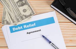 Debt Relief Agreement mit Kugelschreiber, Dollar Geldscheinen, Notizbuch und Lesebrille auf einem Holztisch