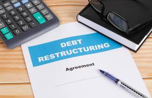 Debt Restructuring mit Kugelschreiber, Dollar Geldscheinen, Notizbuch und Lesebrille auf einem Holztisch