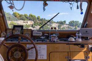 Decorated steering room with wooden steering wheel, of a ship on Greek waters with view of a rocky coast