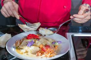 Dekorierte Essen: Frau isst Kabeljau-Fisch, mit lila und roten Blumen verziert, auf einem weißen Teller