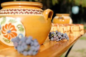 Dekorierte Keramikgefäße für Traubenmost, frische Weintrauben und Tassen auf dem Tisch