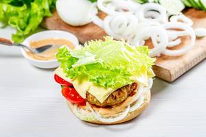 Delicious fresh homemade burger with lettuce, cheese, onion and tomato on a white wooden background (Flip 2019)