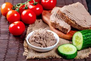Delicious pate in a bowl and on sandwiches on the table with tomatoes and cucumbers