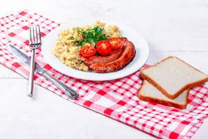 Delicious porridge with sausages and bread with dish towel on white wooden background