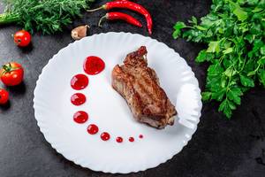 Delicious roasted meat with berry sauce, herbs and chili on a black background