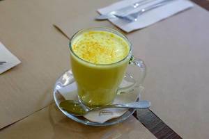 Der Kurkuma-Drink mit Ingwer "Goldene Milch" in einem Glas mit Henkel und kleinem Löffel im veganen Petit Brot Restaurant in Barcelona, Spanien