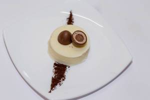 Dessertteller mit Panna Cotta, dekoriert mit halbierter Mozartkugel und Schokoladenpulver