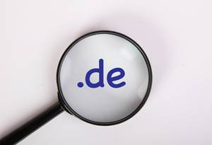 Deutsche Domainendung .de in blau auf weiß, vergrößert dargestellt unter einer Lupe