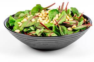Diät-Rezepte: frischer Salat mit Spinat und Pinienkernen in einem schwarzen Teller vor weißem Hintergrund