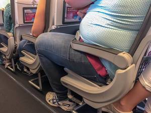 Dicker Fluggast mit wenig Platz auf dem Sitz im Flugzeug