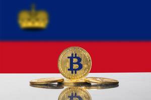 Die Flagge von Lichtenstein mit vier goldenen Bitcoin-Münzen im Vordergrund