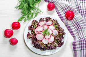Diet salad with radishes and lettuce on a white wooden background. The view from the top