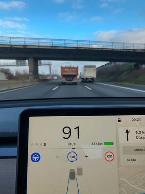 Display of a Tesla car on autopilot mode showing current speed, remaining estimated range, speed limit and presence of vehicles on motorway lanes