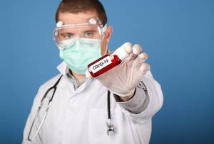 Doctor holding blood sample tube with Covid-19 text on blue background
