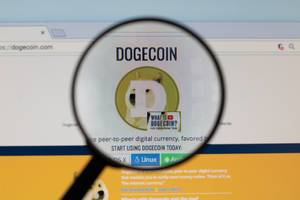 Dogecoin-Logo am PC-Monitor, durch eine Lupe fotografiert