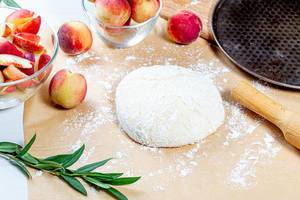 Dough, flour and fresh peaches with rolling pin and baking sheet on the table