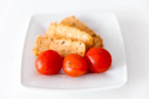Drei gewaschene Tomaten auf einem weißen Teller, vor dem mediterranen Bio-Fleischersatz "Tofu Rosso" von Taifun
