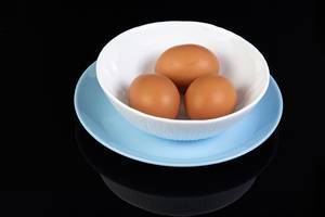 Drei hartgekochte Eier mit Schale in weißer Schale isoliert vor schwarzem Hintergrund