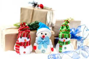 Drei kleine Schneemänner mit Mütze und Schal vor Weihnachtsgeschenken im Schnee