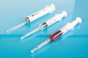 Drei Spritzen mit Sicherheitsdeckeln auf den Nadeln und Blutprobe