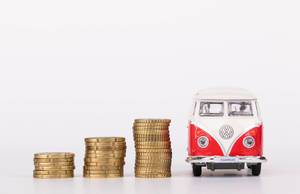 Drei Stapel Münzen und VW-Bulli-Spielzeug auf weißem Hintergrund