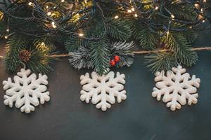Drei weisse Schneeflocken mit Weihnachtsbaum Ästen und Leuchtgirlanden auf dunklem Hintergrund