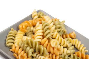Dreifarbige, gekochte Fusilli Pasta al dente auf grauem Teller vor weißem Hintergrund