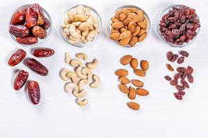 Dried dates, raisins, cashew nuts and almonds on white wooden background