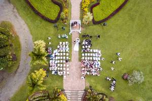 Drohnenaufnahme einer Hochzeit im Garten einer alten Villa, Brautpaar schreitet zum Traualtar