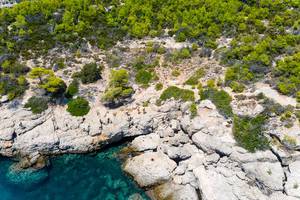 Drohnenaufnahme zeigt Touristen auf einer Gesteinsküste, beim Erkunden der Sehenswürdigkeit Bekiris Höhle, auf der saronischen Insel Spetses