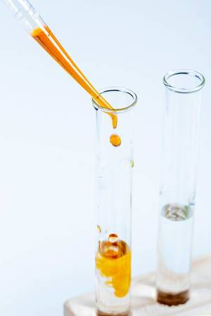 Drops of orange liquid fall into a glass laboratory tube