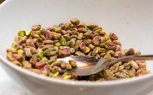 Dry-roasted pistachios with spoon in white bowl