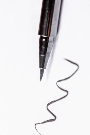 Dunkler Eyeliner mit Präzisionspinsel zeichnet Linie auf weißem Untergrund