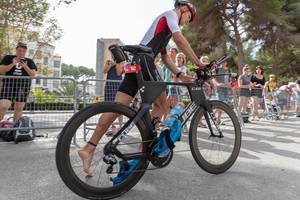 Dynamische Quersicht - Ein Sportler mit Nummer 112 besteigt sein Rad beim Challenge Triathlon in Peguera