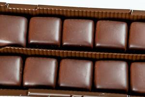 Eckige Süßigkeiten mit Schokoladenglasur in Kunststoffverpackung vor weißem Hintergrund