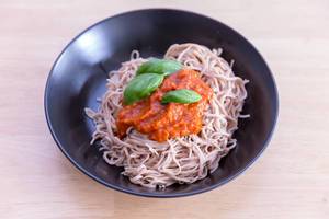 Edemama Bio-Spaghetti made from azuki beans with tomatosauce and basil leaves on a black plate