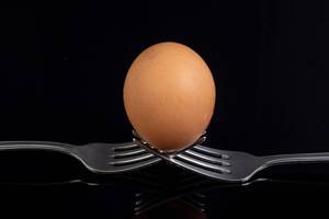 Egg sitting on the crossed forks above black background