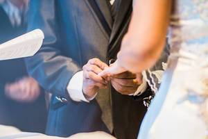 Ehemann steckt bei Hochzeit Ehering an Finger der Braut und besiegelt die Eheschließung
